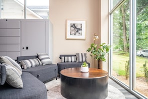 A modern living room with grey sofas, striped cushions, a round coffee table, and a large window offering a view of the outdoors. - Stylish 1B1B with Modern Finishes (Atlanta)
