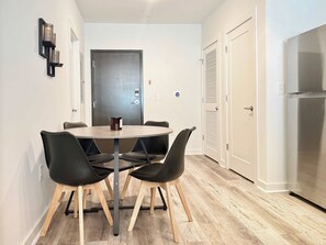 Eine moderne Küche mit einem Edelstahl-Kühlschrank, einer Essecke mit einem runden Tisch und vier Stühlen sowie einer Tür mit Griff.