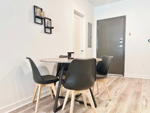 A dining area with a round table, four black chairs, and a coffee cup. There are wooden chairs with metal legs, a white door, and a dark door in the background. - Stylish 1B1B with Modern Finishes (Atlanta)