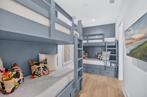 A bunk bed room with a built-in desk and shelving, a window with a view of the beach, and a painting of a sunset. - Good Tides: Private Beach, Heated Pool & Spa, Free Golf Cart, 5,700+ SqFt (Miramar Beach)