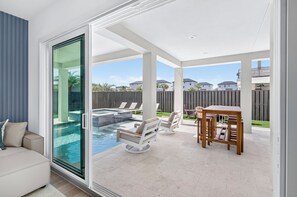 A modern living room with a glass door leading to a patio area featuring a hot tub, lounge chairs, and a wooden table. - Good Tides: Private Beach, Heated Pool & Spa, Free Golf Cart, 5,700+ SqFt (Miramar Beach)