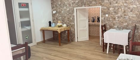 Una habitación con pared de piedra, una mesa de madera con mantel, sillas y una puerta con señal de emergencia.