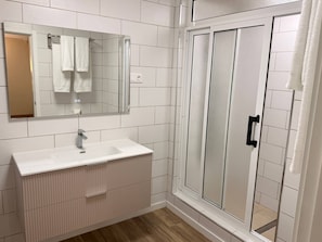 A bathroom with a white sink, mirror, and a glass shower enclosure.