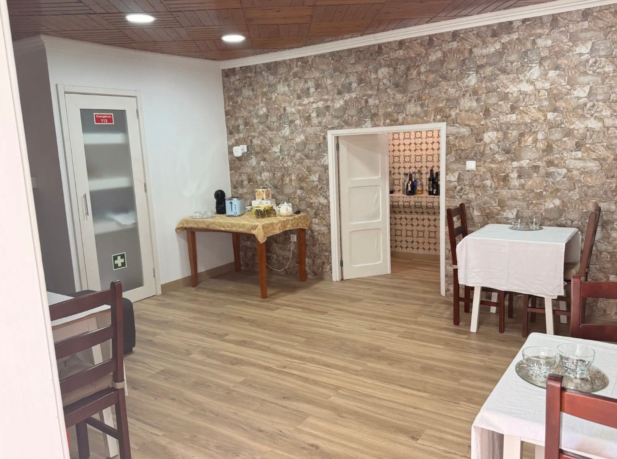 Una habitación con pared de piedra, una mesa de madera con mantel, sillas y una puerta con señal de emergencia.