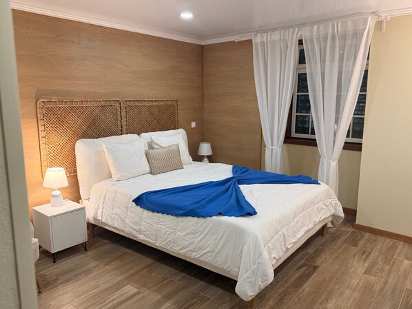 A neatly made bed with a blue blanket, a bedside lamp, and a nightstand.
