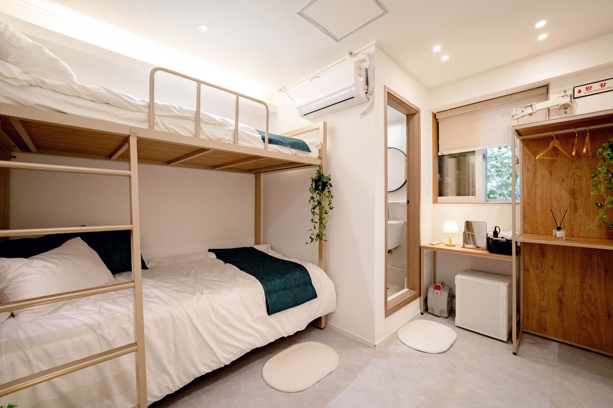Habitación con literas, un escritorio, un espejo, un radiador pequeño y una planta.