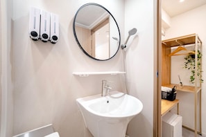 Un baño con lavamanos blanco, un espejo y una ducha con cabezal de ducha manual.
