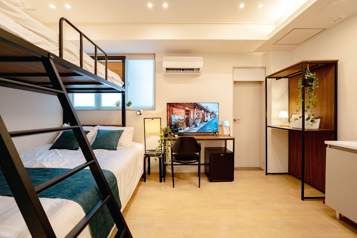 Habitación de hotel compacta con literas, un escritorio con computadora, televisión y una pequeña zona de estar.