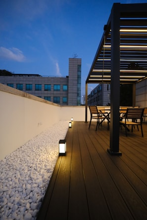 Une terrasse sur le toit, dotée d’une plateforme en bois, d’un espace salon et offrant une vue sur les bâtiments en arrière-plan.