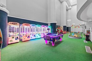 A room with arcade games, a small play area, and a wall with a hexagonal pattern. - ☀️Ocean Front Condo with Expansive Views-Daytona Ocean Walk Resort 706☀️ (Daytona Beach)