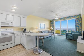 Cocina compacta con electrodomésticos modernos, comedor con sofá y mesa, y balcón con vistas.
