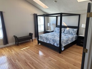 A four-poster bed with a floral bedspread, a bedside table with a lamp, a bench, and a window with curtains. - Spacious 4-bedroom house in Castle Pines Cul de sac with walk out basement (Castle Pines)