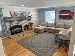A living room with a fireplace, a sectional sofa, a patterned rug, and artwork on the walls. - Spacious 4-bedroom house in Castle Pines Cul de sac with walk out basement (Castle Pines)