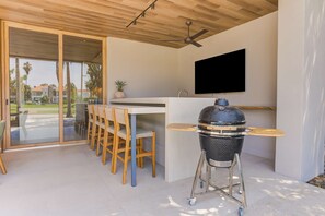 A modern kitchen with a built-in grill, a flat-screen TV, and a dining area with chairs. - El Tigre Luxury Golf Villa w/ Pool & Beach Club (Nuevo Nayarit)
