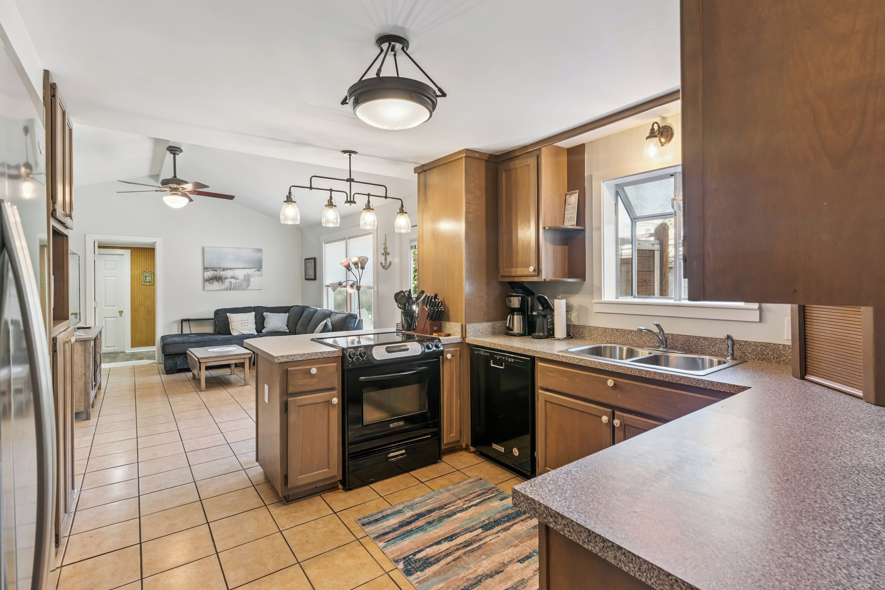 A modern kitchen with a central island, built-in oven, dishwasher, and a large window.