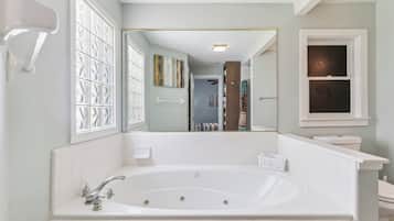A bathroom with a large bathtub, a toilet, and a window with frosted glass.