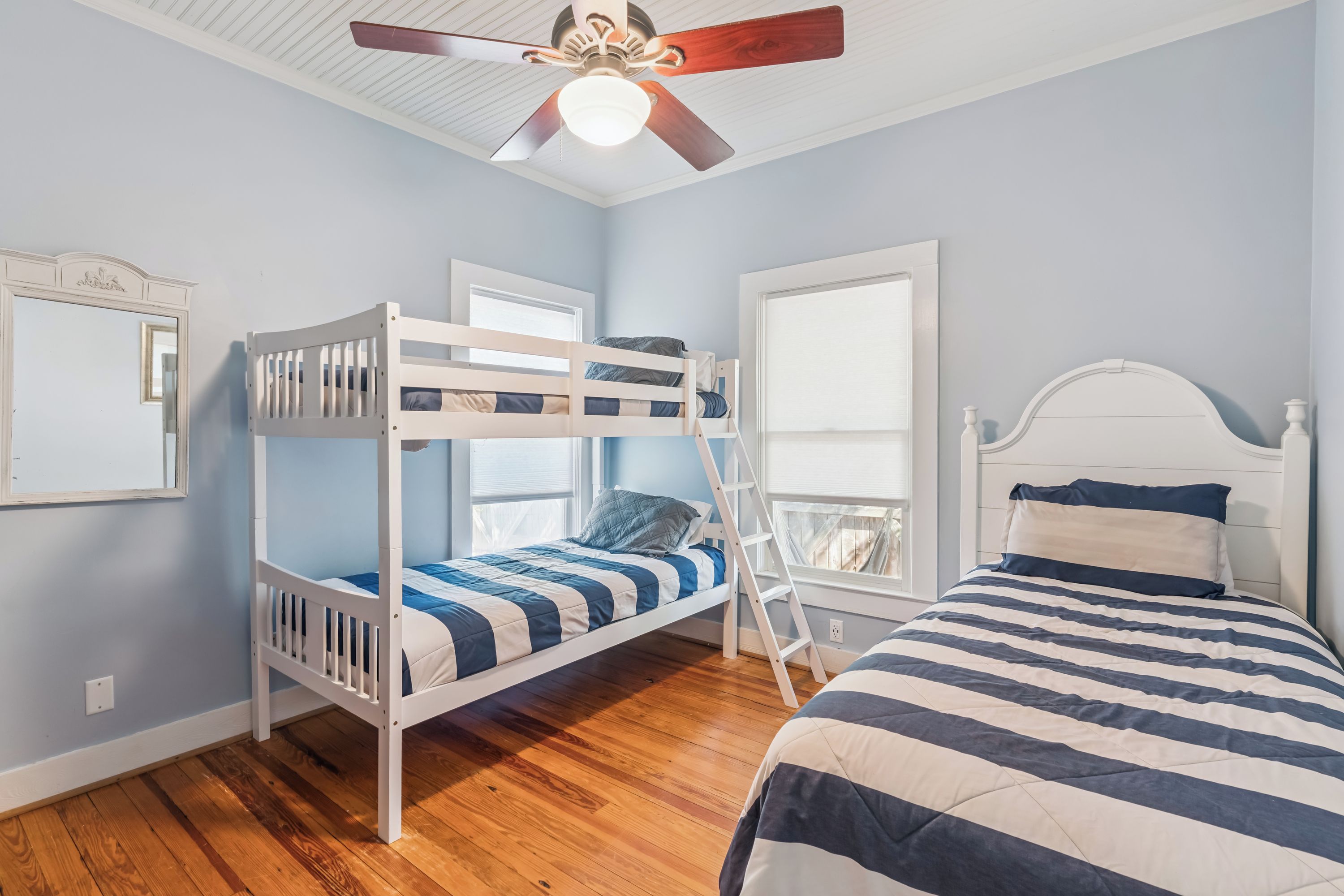 Una habitación con literas, una cama individual, ventilador de techo y una ventana con persianas.