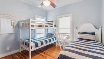 Una habitación con literas, una cama individual, ventilador de techo y una ventana con persianas.