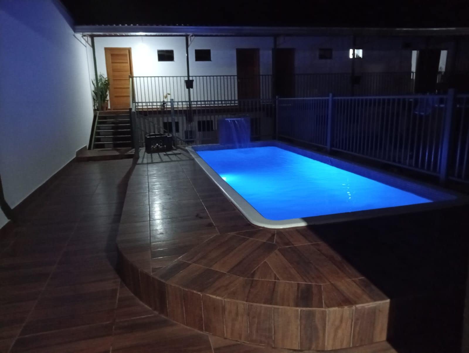 Una piscina con bordo piastrellato e una piccola scalinata che conduce a una porta.