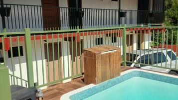 A swimming pool with a tiled edge, a covered patio area with a metal roof, and a green fence surrounding the property.