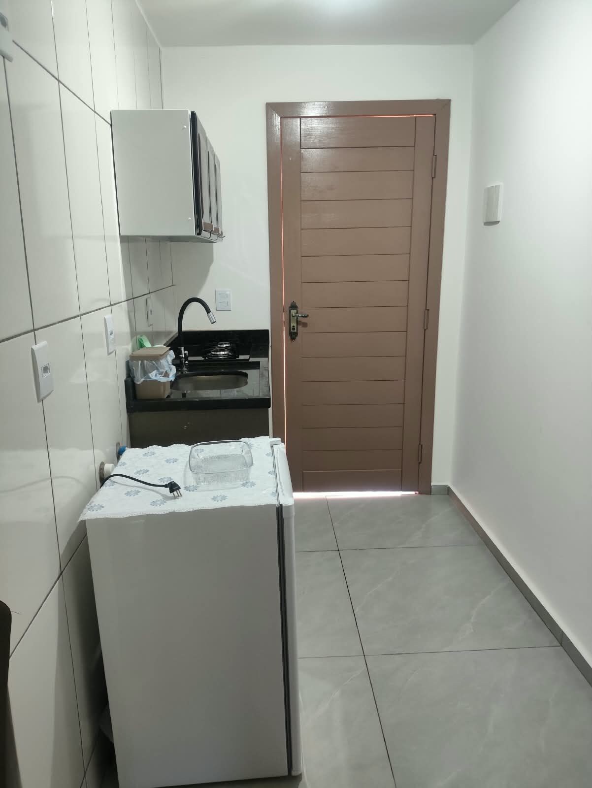 Una cocina compacta con alacenas blancas, un refrigerador y una puerta.