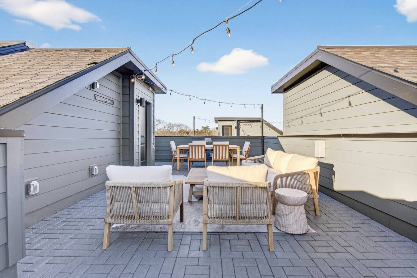 A rooftop patio with outdoor furniture, a string of lights, and a view of the surrounding buildings.