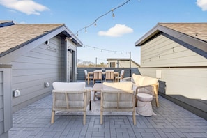 A rooftop patio with outdoor furniture, a string of lights, and a view of the surrounding buildings. - Rooftop with Dining, Walk to Restaurants and Brewery (Nashville)