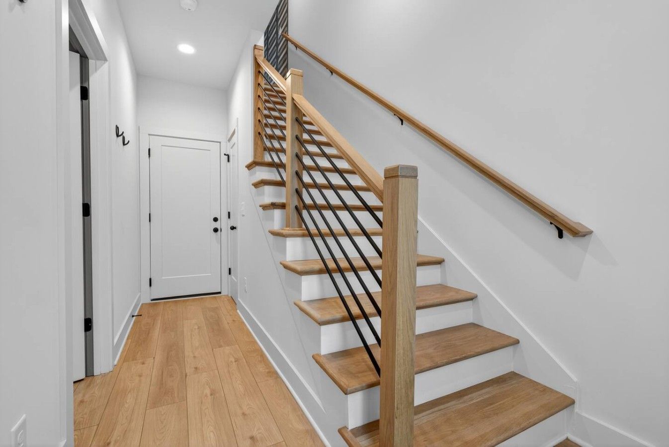 A staircase with wooden steps and a black handrail, leading to a white door at the top.