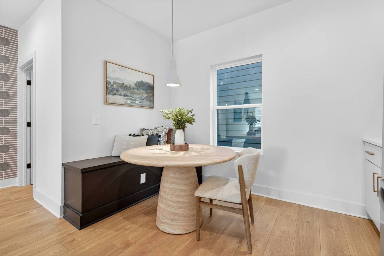 A modern dining area with a round table, a bench, and a window with blinds.