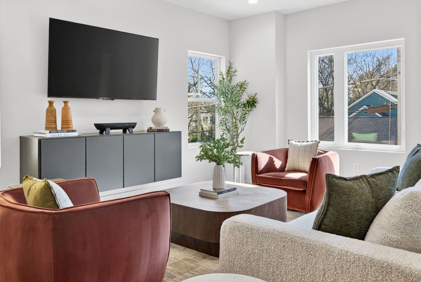 A modern living room with a flat-screen TV, a grey sofa, a red armchair, and a coffee table.