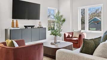 A modern living room with a flat-screen TV, a grey sofa, a red armchair, and a coffee table.