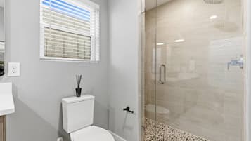 A bathroom with a toilet, a glass-enclosed shower, and a window with blinds.