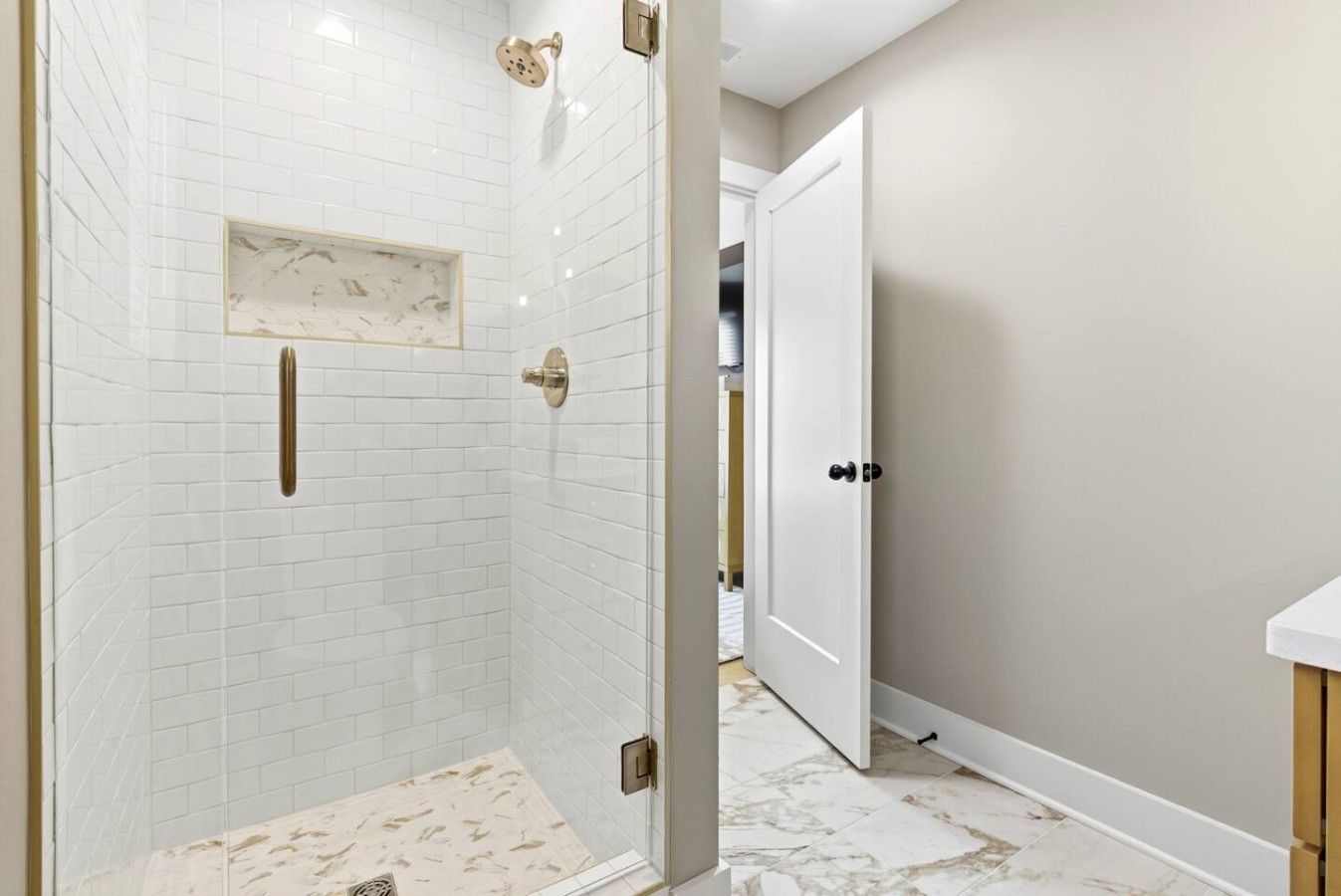 A bathroom with white subway tiles, a shower with a glass door, and a white door leading to another room.