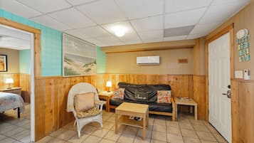 A cozy room with a wooden floor, a sofa, a wicker chair, a small table, and a painting on the wall.