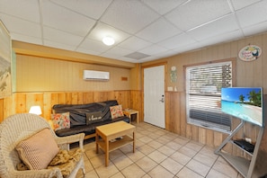 A cozy room with a wooden panel wall, a black leather sofa, a wicker chair, a small wooden table, and a television on a stand. - BC6--1 BR/1 Bath Condo, Pool, Walk to Beach, Sleeps 2 Adults/2 Kids, Dog OK! (Port Aransas)