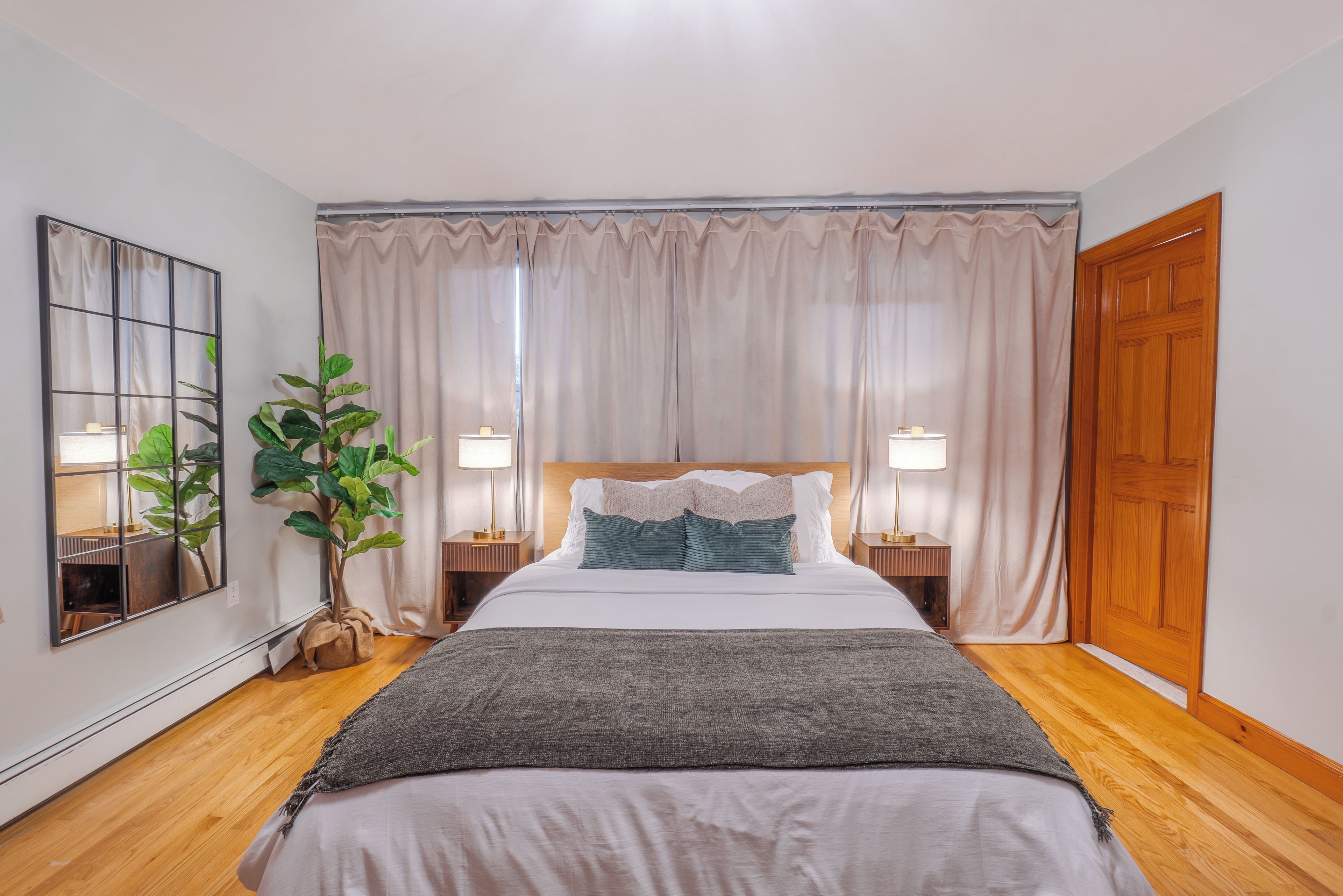 A neatly arranged bedroom with a large bed, a potted plant, and a wooden door.