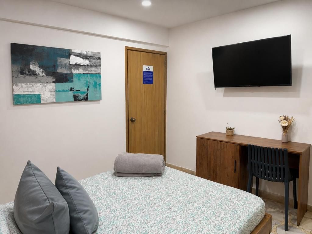 Ett sovrum med en säng, ett skrivbord, en stol, en tv och en tavla på väggen.