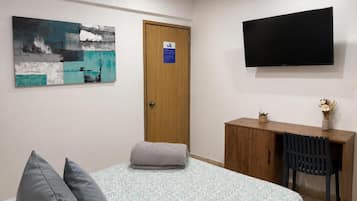 Ett sovrum med en säng, ett skrivbord, en stol, en tv och en tavla på väggen.