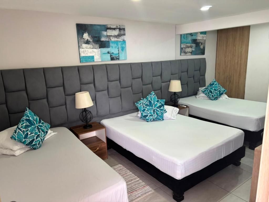 Une chambre d’hôtel avec deux lits, une tête de lit grise en tissu et des œuvres d’art abstraites accrochées au mur.
