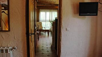 Een gang met betegelde vloer, een houten deur, een radiator en een televisie aan de muur.