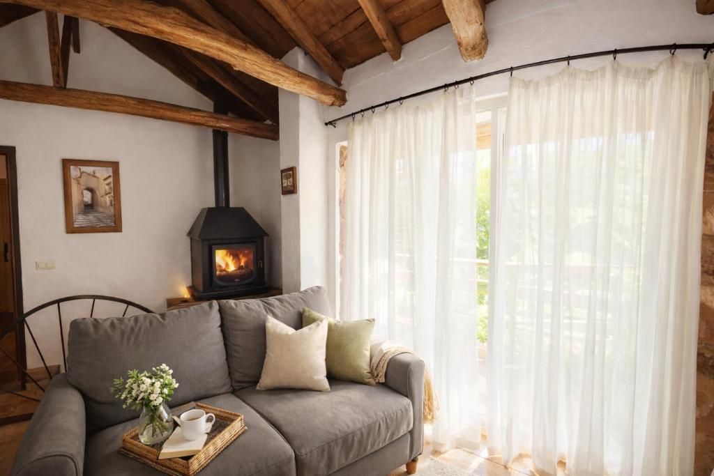 A cozy living room with a sofa, a fireplace, and a large window with sheer curtains.