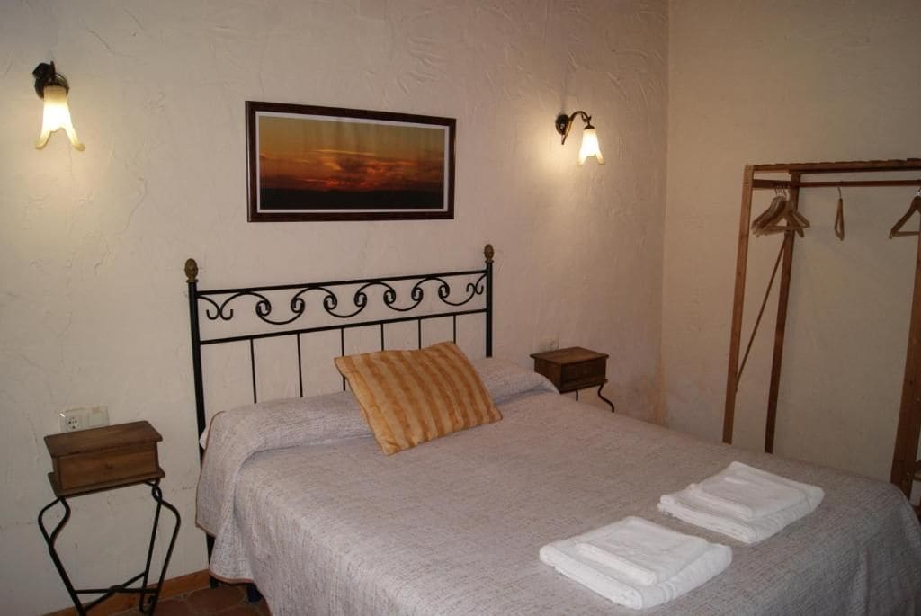 Un dormitorio con una cama, una mesita de noche, un cuadro en la pared y un perchero.