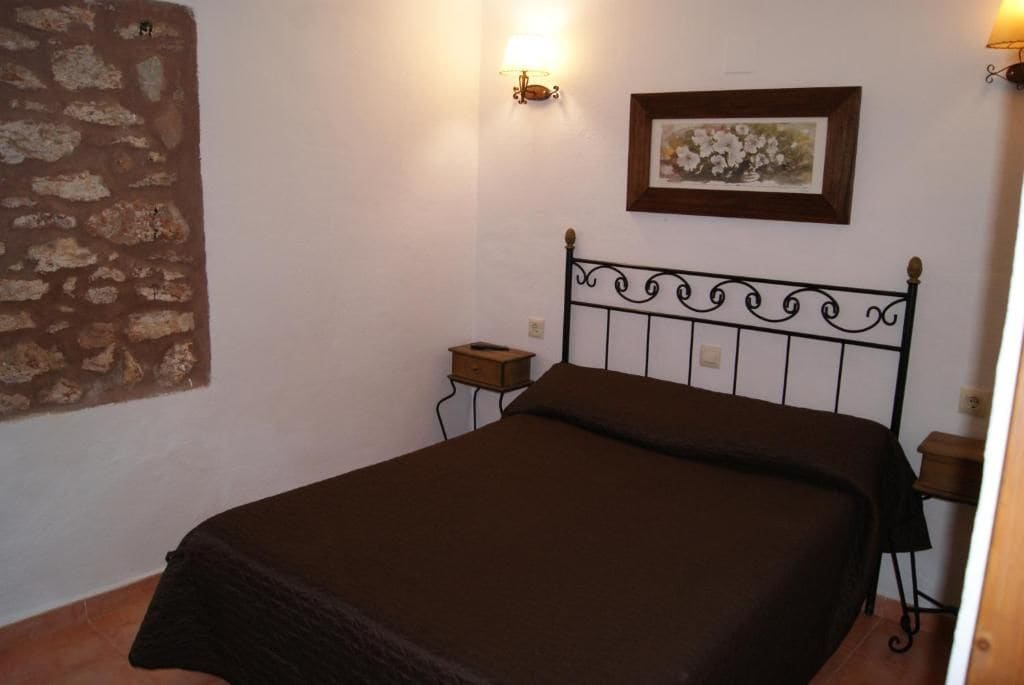 Una cama individual con cabecera de metal, una mesita de noche, una lámpara de pared y un cuadro enmarcado.