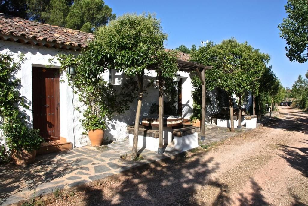Un bâtiment rustique avec un toit en tuiles, une porte en bois et un chemin de pierre menant à un espace extérieur abrité, aménagé pour s’y asseoir.