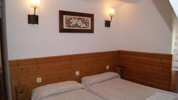 A room with two beds, wooden headboard, wall-mounted light fixtures, and a framed picture.