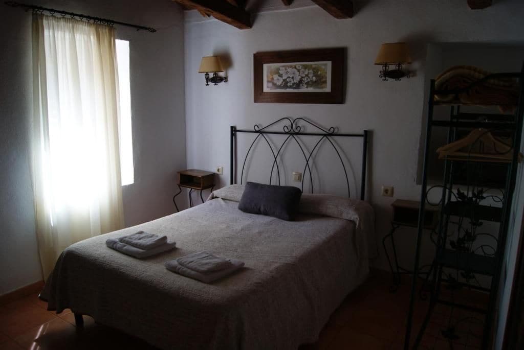A bedroom with a bed, a nightstand, a wall-mounted lamp, a framed picture, and a metal rack.