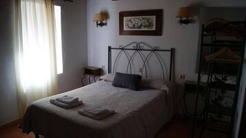 A bedroom with a bed, a nightstand, a wall-mounted lamp, a framed picture, and a metal rack.