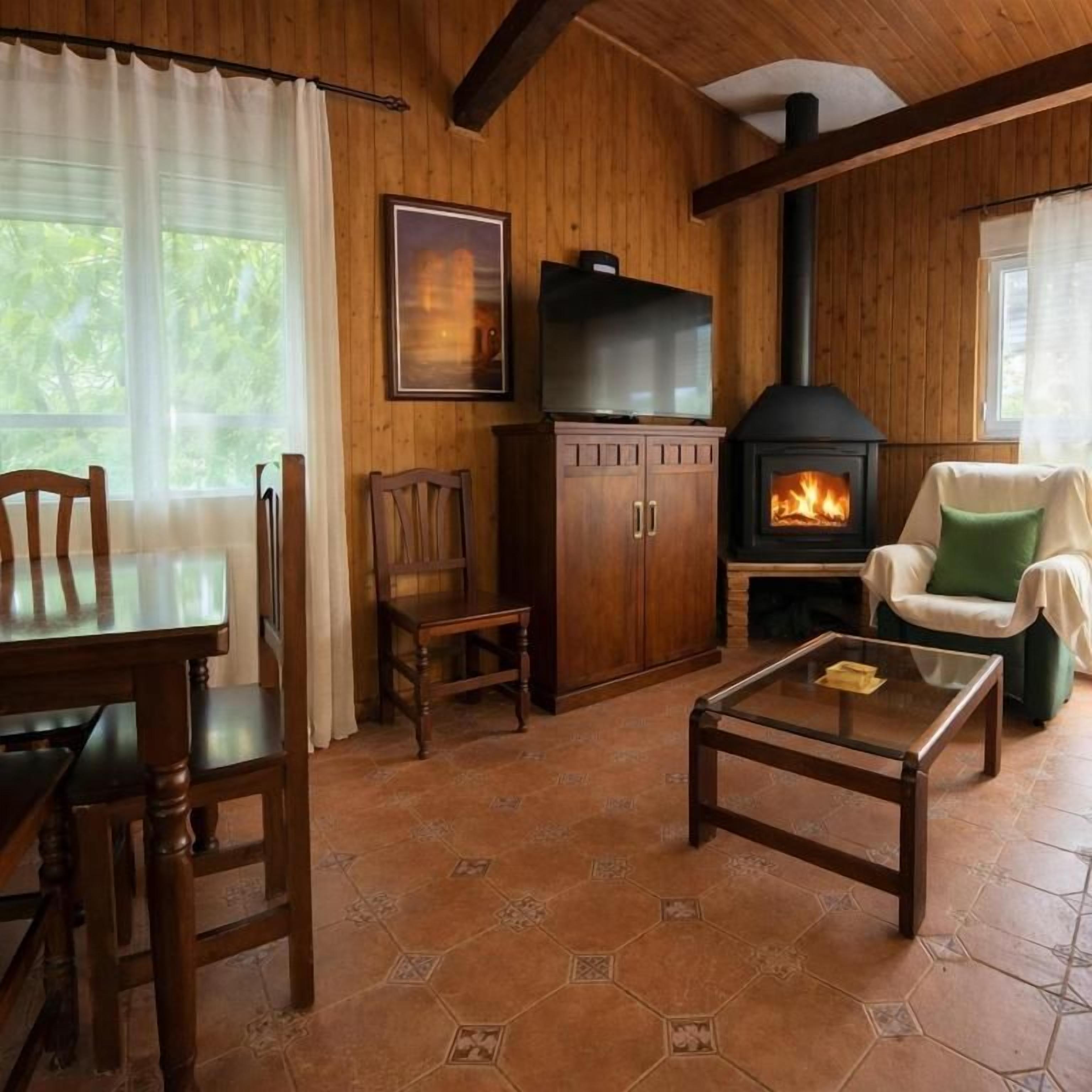 A cozy room with a wooden interior, a fireplace, a dining table with chairs, and a sofa.