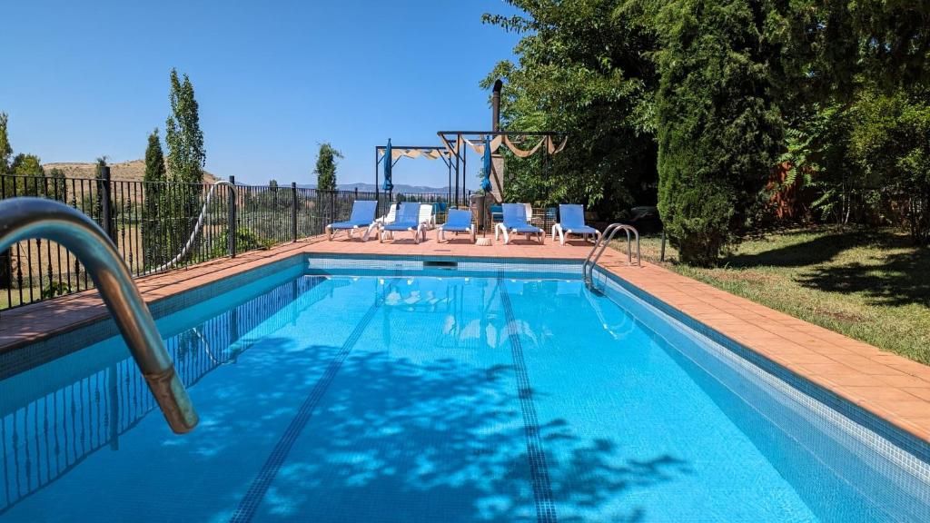 Una piscina con escalera metálica, rodeada por una cerca y protegida por árboles.