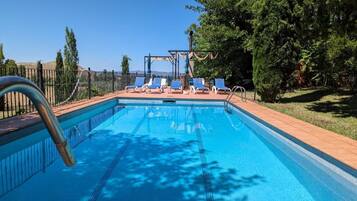 Una piscina con escalera metálica, rodeada por una cerca y protegida por árboles.